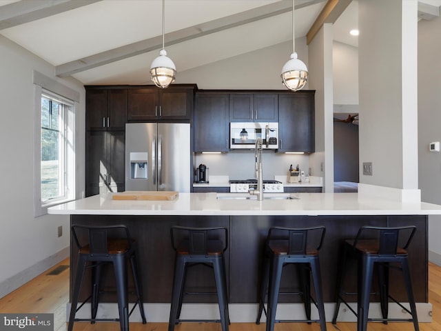 kitchen featuring appliances with stainless steel finishes, vaulted ceiling with beams, dark brown cabinetry, and a kitchen bar