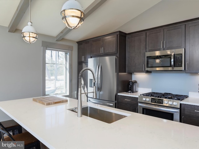 kitchen featuring dark brown cabinetry, hanging light fixtures, stainless steel appliances, a kitchen bar, and a sink