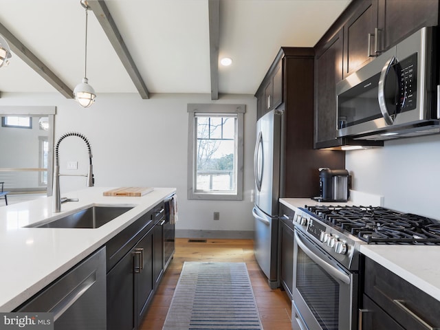 kitchen with light wood-style flooring, stainless steel appliances, a sink, light countertops, and beam ceiling