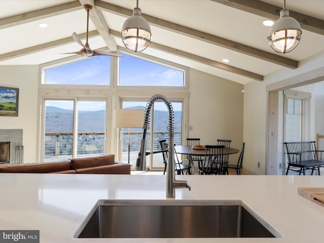 kitchen with open floor plan, vaulted ceiling with beams, hanging light fixtures, a mountain view, and a sink