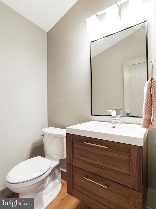 half bathroom with vanity, toilet, and wood finished floors