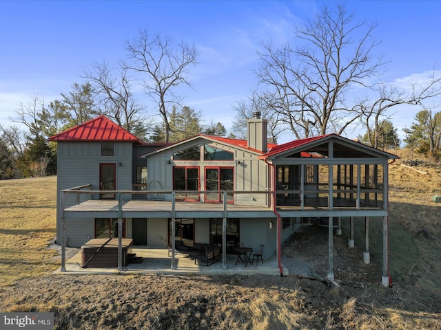 back of house featuring a hot tub, a chimney, metal roof, a standing seam roof, and a patio area