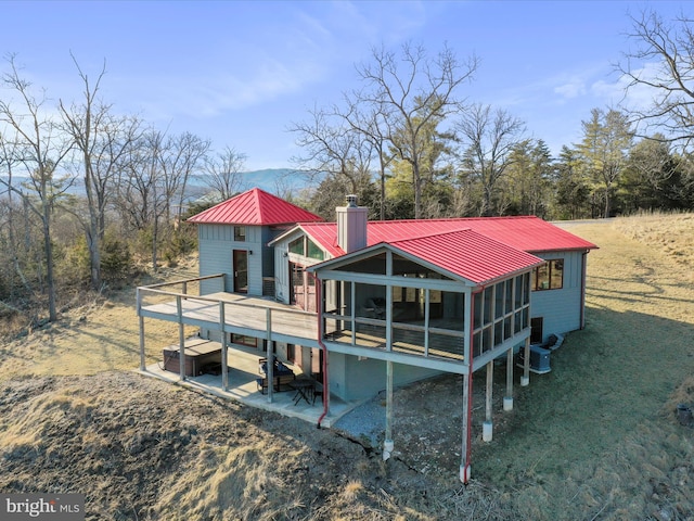 back of property featuring a patio, a chimney, a sunroom, metal roof, and a deck