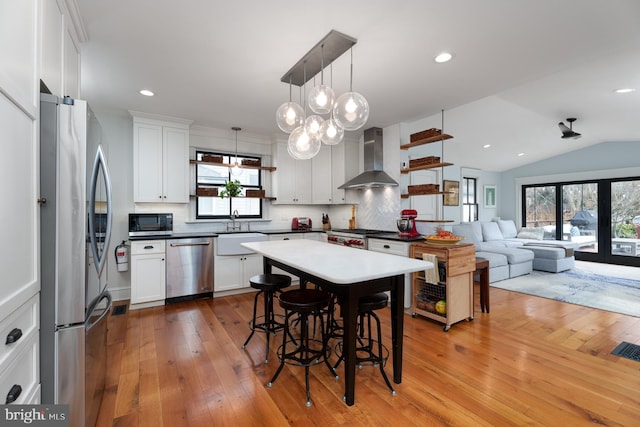 kitchen featuring stainless steel appliances, a breakfast bar, a sink, decorative backsplash, and wall chimney exhaust hood