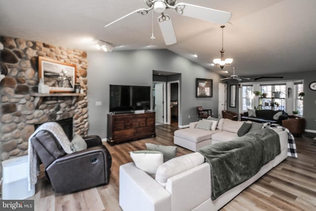 living room with vaulted ceiling, ceiling fan with notable chandelier, hardwood / wood-style floors, and a fireplace