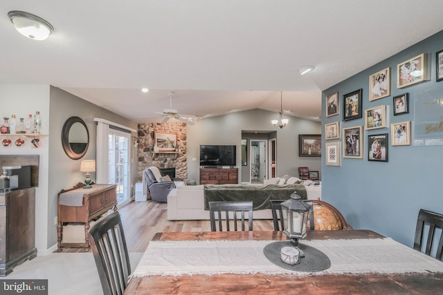 dining area featuring vaulted ceiling, light wood-type flooring, ceiling fan with notable chandelier, and a fireplace