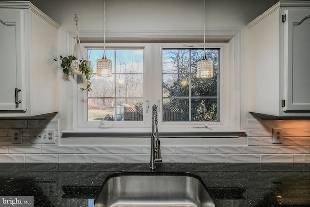 interior details featuring pendant lighting, sink, dark stone countertops, white cabinets, and backsplash