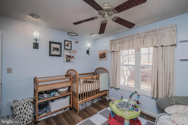 bedroom with ceiling fan, dark wood-type flooring, a nursery area, and a textured ceiling