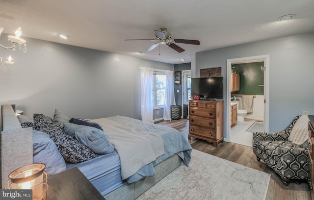 bedroom featuring dark hardwood / wood-style floors, ceiling fan with notable chandelier, and ensuite bath