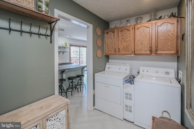 laundry area with light parquet floors, washing machine and dryer, cabinets, and a textured ceiling