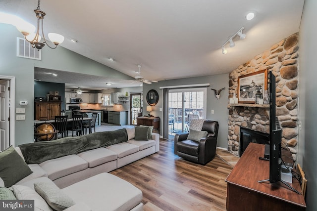 living room featuring ceiling fan with notable chandelier, lofted ceiling, hardwood / wood-style floors, and a stone fireplace