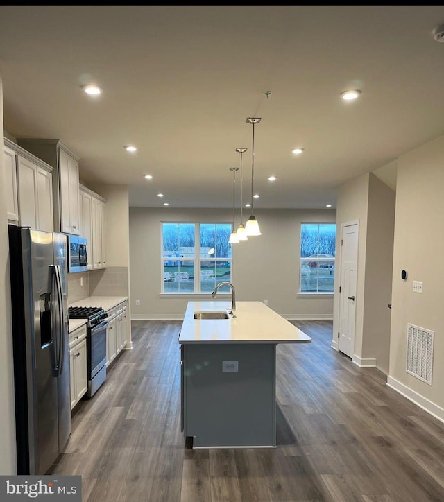 kitchen with sink, white cabinetry, hanging light fixtures, stainless steel appliances, and a center island with sink