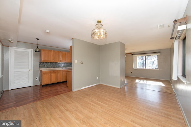 kitchen with pendant lighting, sink, tasteful backsplash, light hardwood / wood-style floors, and a chandelier