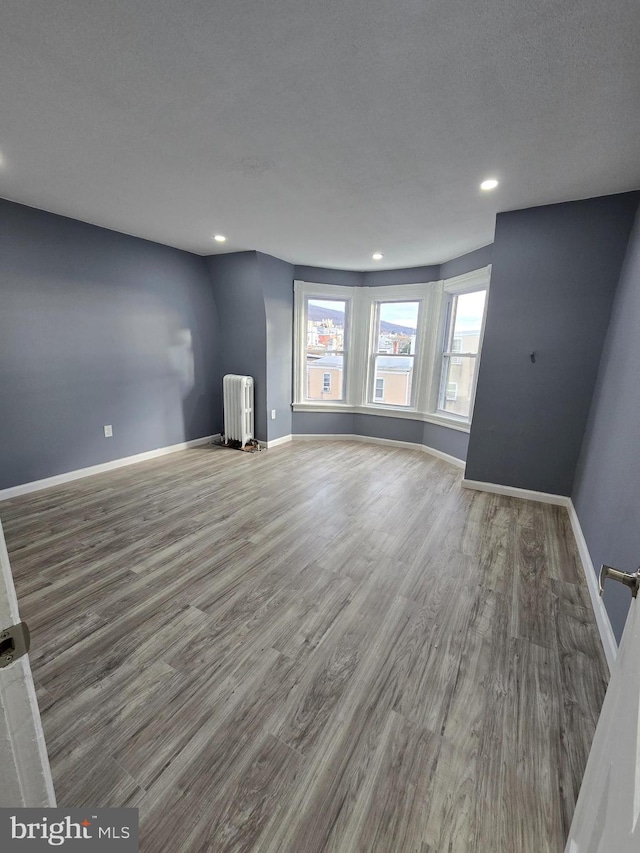 unfurnished living room with hardwood / wood-style flooring, radiator heating unit, and a textured ceiling