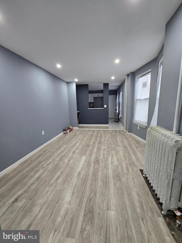 unfurnished living room featuring radiator heating unit and light hardwood / wood-style floors