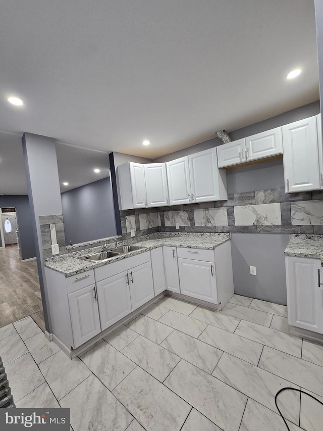 kitchen with sink, light stone counters, kitchen peninsula, white cabinets, and backsplash