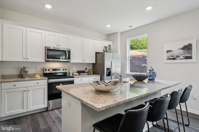 kitchen with a kitchen breakfast bar, an island with sink, stainless steel appliances, light stone countertops, and white cabinets