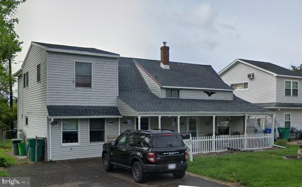 view of front facade featuring covered porch, roof with shingles, and a chimney