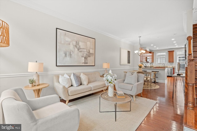 living room featuring hardwood / wood-style flooring, ornamental molding, sink, and an inviting chandelier