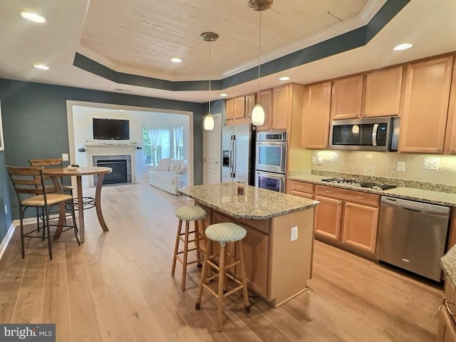 kitchen with light hardwood / wood-style flooring, appliances with stainless steel finishes, hanging light fixtures, a tray ceiling, and light stone countertops