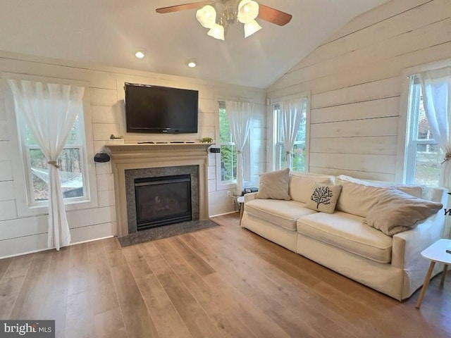 living room with vaulted ceiling, hardwood / wood-style floors, a fireplace, wood walls, and ceiling fan