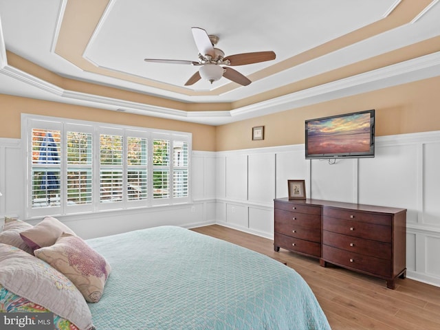 bedroom with a raised ceiling, ceiling fan, and light wood-type flooring