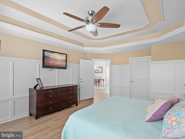 bedroom with a raised ceiling, ornamental molding, ceiling fan, and light wood-type flooring