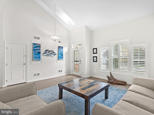 living room featuring hardwood / wood-style flooring, high vaulted ceiling, a chandelier, and a skylight