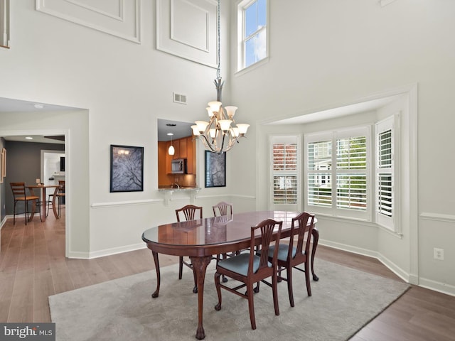 dining area with an inviting chandelier, a towering ceiling, light hardwood / wood-style flooring, and a healthy amount of sunlight