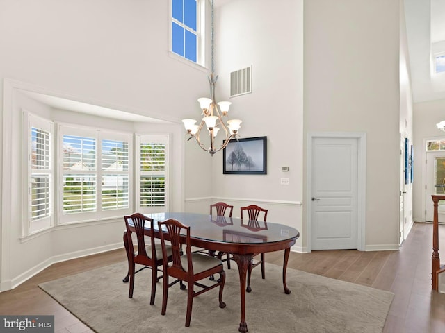 dining area with hardwood / wood-style flooring, a towering ceiling, and a chandelier