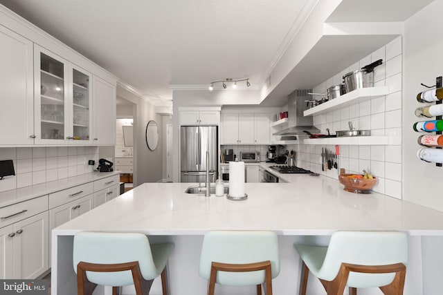 kitchen featuring stainless steel fridge, a breakfast bar, white cabinetry, kitchen peninsula, and wall chimney exhaust hood