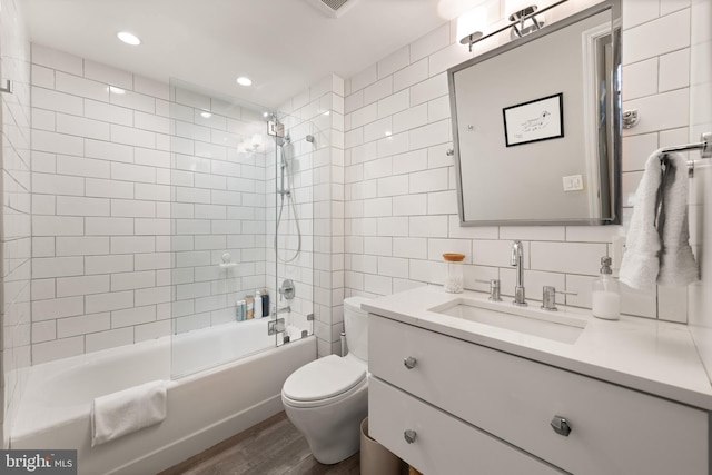 full bathroom with tile walls, vanity, wood-type flooring, tiled shower / bath, and toilet