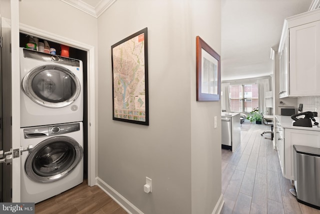 laundry room featuring crown molding, hardwood / wood-style flooring, and stacked washing maching and dryer