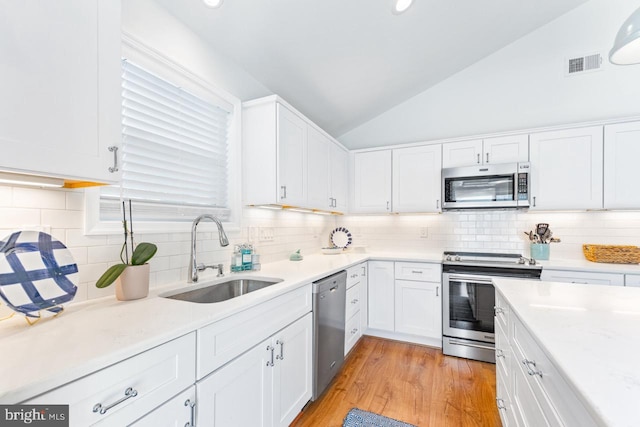 kitchen featuring appliances with stainless steel finishes, lofted ceiling, sink, white cabinets, and light hardwood / wood-style flooring