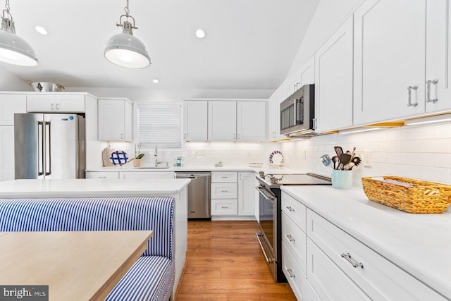 kitchen with sink, hanging light fixtures, light wood-type flooring, appliances with stainless steel finishes, and white cabinets