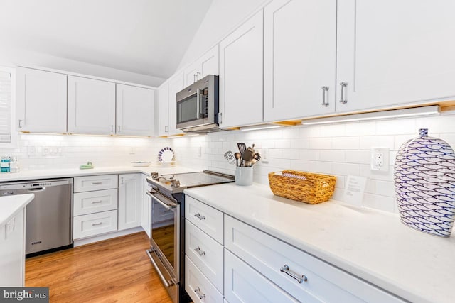 kitchen with lofted ceiling, appliances with stainless steel finishes, white cabinets, and light wood-type flooring