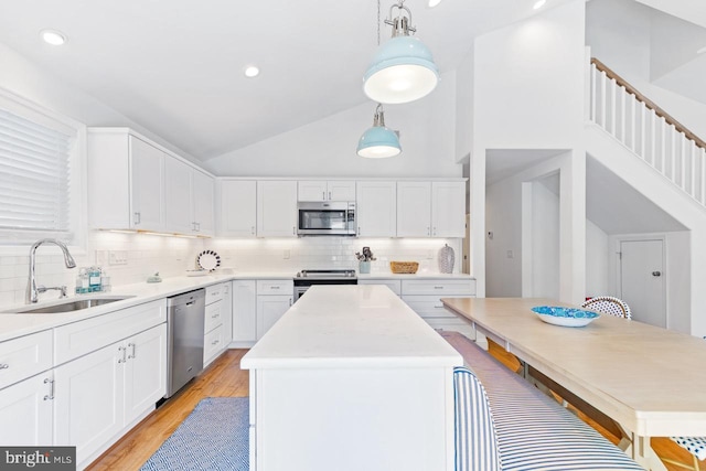 kitchen featuring sink, appliances with stainless steel finishes, white cabinetry, a kitchen island, and decorative light fixtures