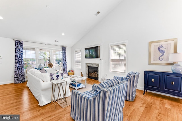 living room with high vaulted ceiling, plenty of natural light, a high end fireplace, and light hardwood / wood-style flooring