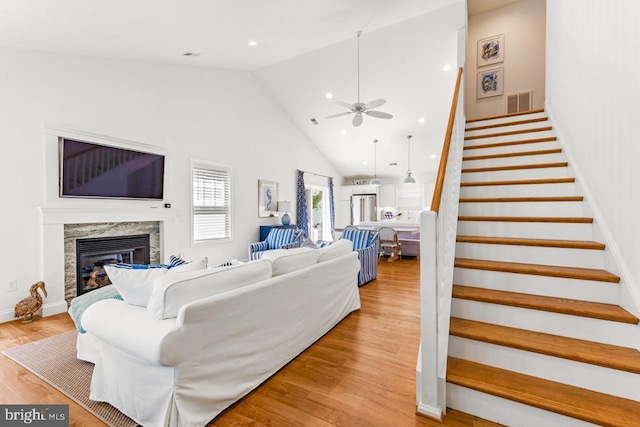 living room with light hardwood / wood-style flooring, a high end fireplace, high vaulted ceiling, and ceiling fan