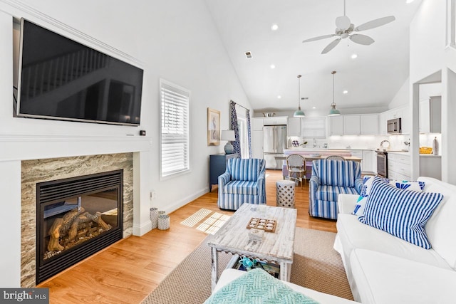 living room with a premium fireplace, high vaulted ceiling, ceiling fan, and light hardwood / wood-style floors