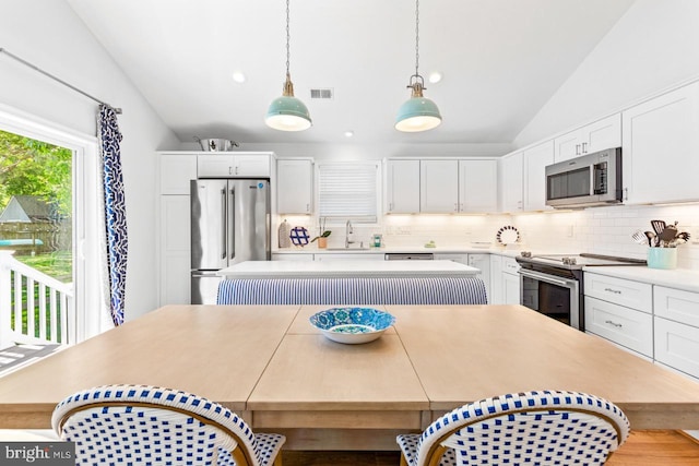 kitchen with lofted ceiling, decorative light fixtures, appliances with stainless steel finishes, breakfast area, and white cabinets