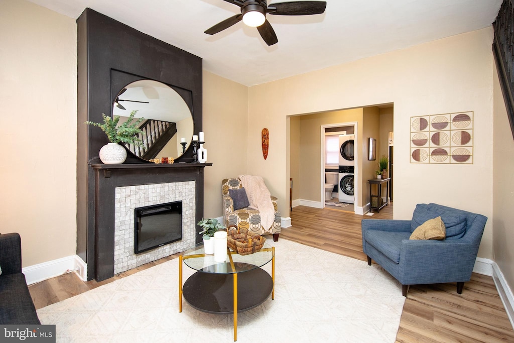 living room featuring ceiling fan, stacked washing maching and dryer, a tiled fireplace, and light hardwood / wood-style flooring