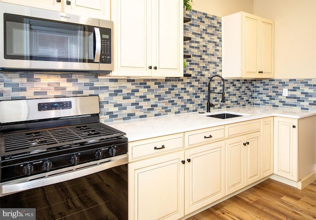 kitchen featuring sink, backsplash, stainless steel appliances, light hardwood / wood-style floors, and cream cabinetry