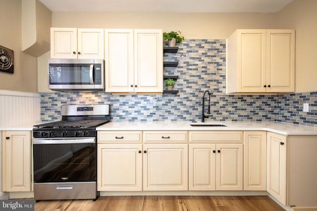 kitchen featuring sink, backsplash, appliances with stainless steel finishes, light hardwood / wood-style floors, and cream cabinetry