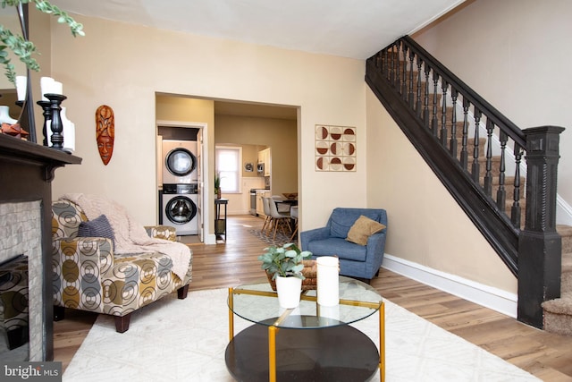 living room featuring stacked washer / drying machine, wood-type flooring, and a brick fireplace