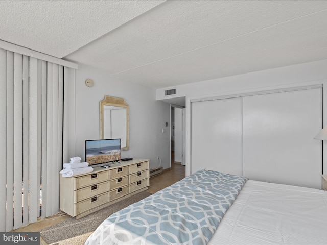 bedroom with a textured ceiling, baseboard heating, and a closet