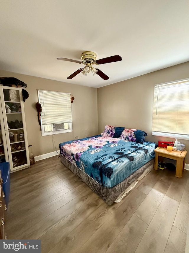 bedroom featuring cooling unit, ceiling fan, wood-type flooring, and multiple windows