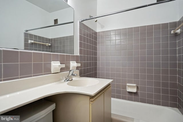 full bathroom featuring tile walls, tiled shower / bath combo, vanity, decorative backsplash, and toilet