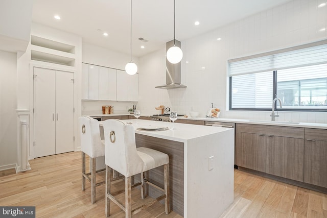 kitchen featuring a kitchen bar, sink, decorative light fixtures, a center island with sink, and white cabinets