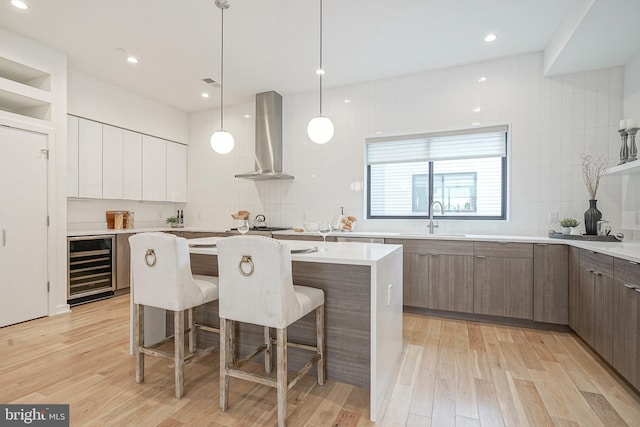 kitchen with wall chimney exhaust hood, sink, a center island, beverage cooler, and white cabinets